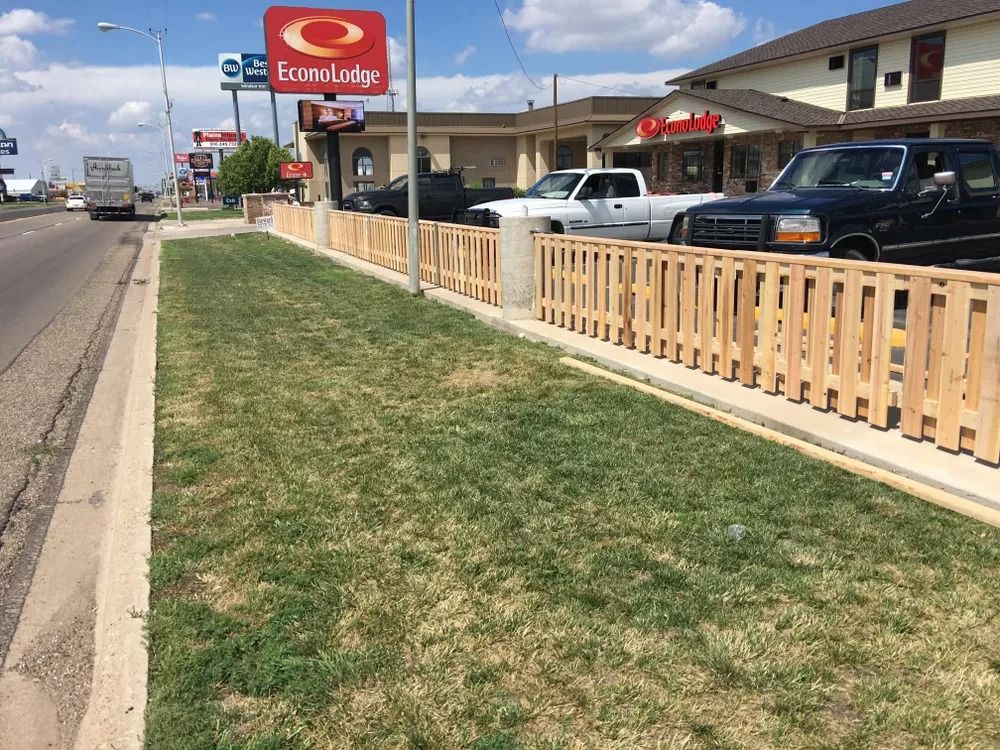 A roadside view with grass, wooden fence, and businesses including a motel and restaurant. Cars drive on the road.