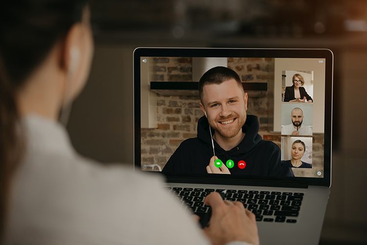 Woman on a video call, laptop screen showing three other participants, smiling.