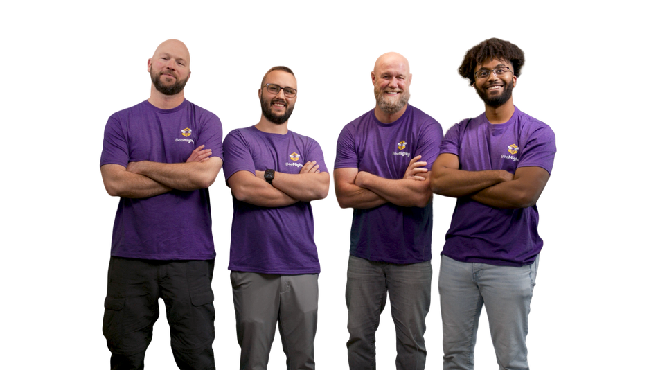 Four men in purple shirts with arms crossed, standing against a white backdrop.