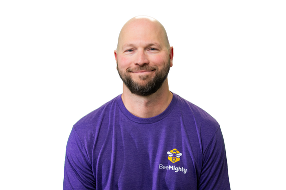 Man with a bald head and beard wearing a purple shirt, smiling, against a white background.
