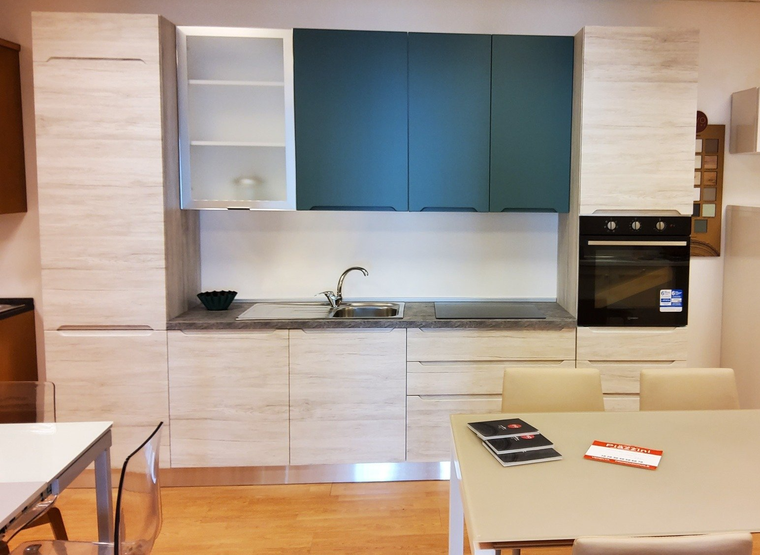 Mobili da cucina moderni: venature del legno chiaro, piano superiore verde acqua, forno incorporato, tavolo da pranzo in primo piano.