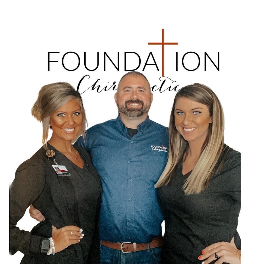 A man and two women pose for a picture in front of the foundation chiropractic logo