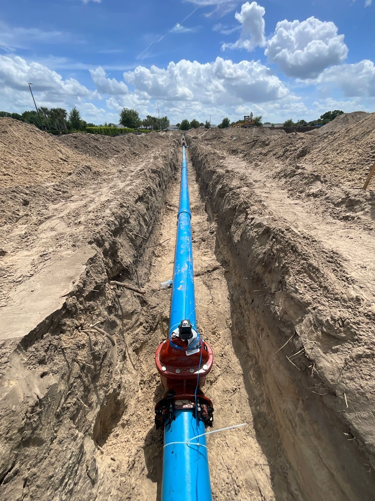 Construction site with an excavator and other machinery, moving earth under a bright blue sky.