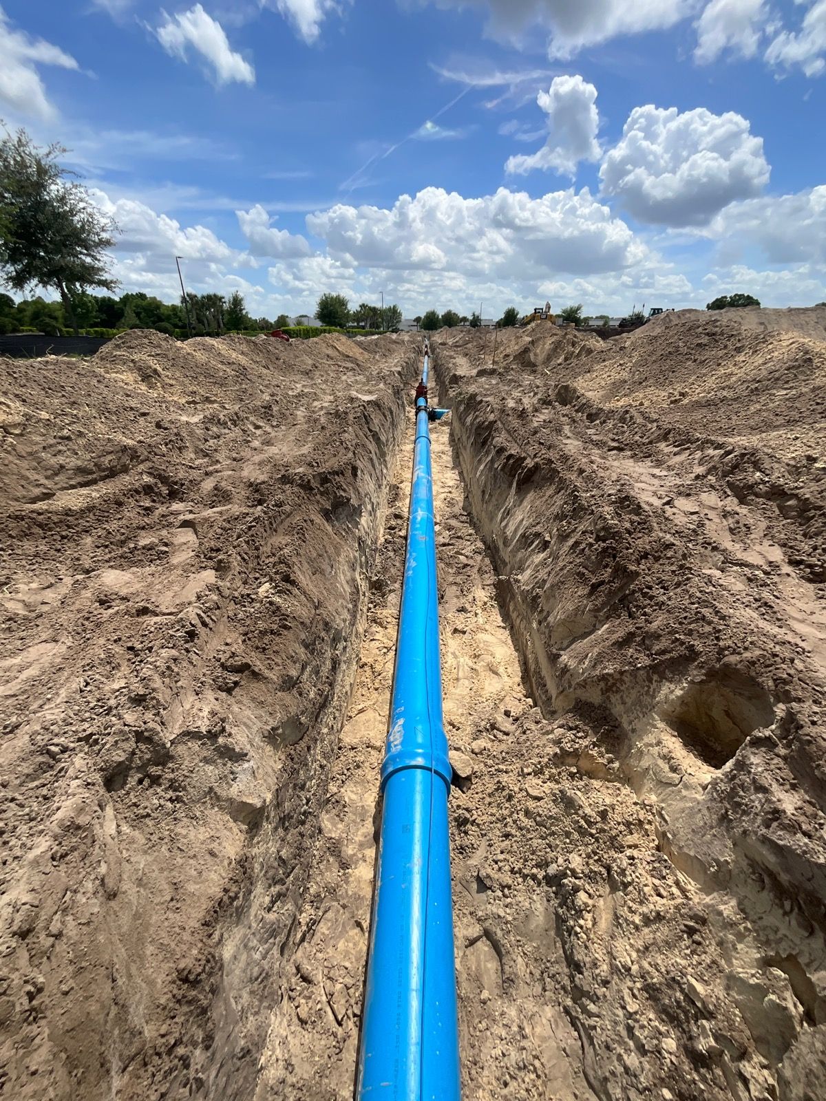 Construction workers in a trench near a road, using equipment and managing electrical cables.