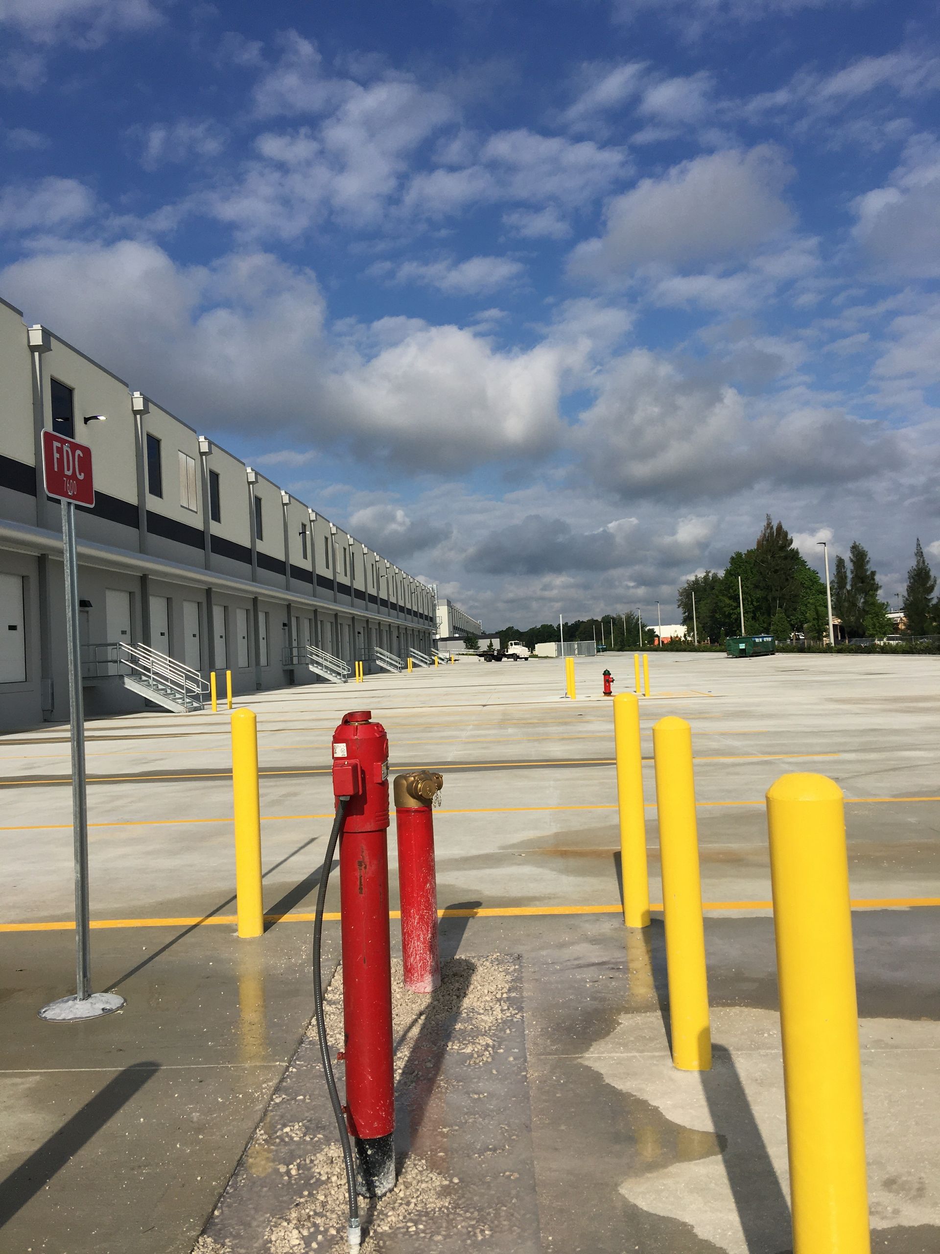 Exterior of a warehouse with loading docks, yellow bollards, red fire hydrants, and a cloudy sky.
