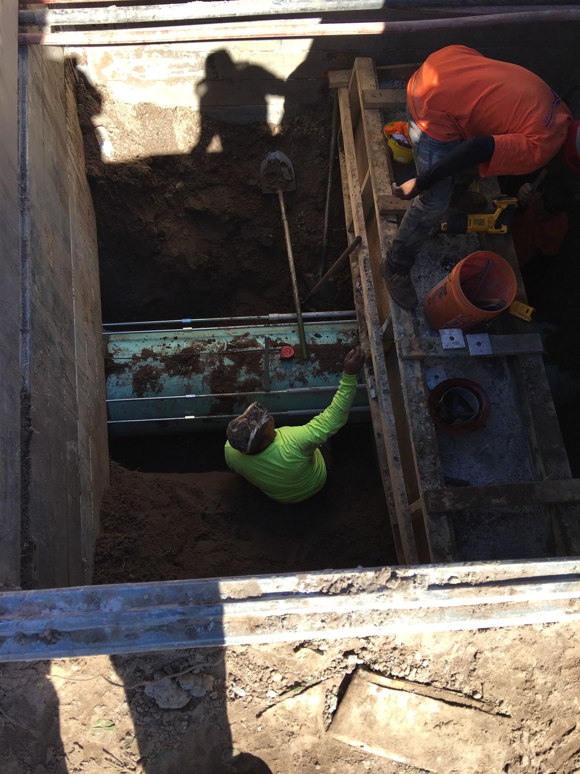 Workers in trench, one wearing neon green, other in orange, working on underground utilities.