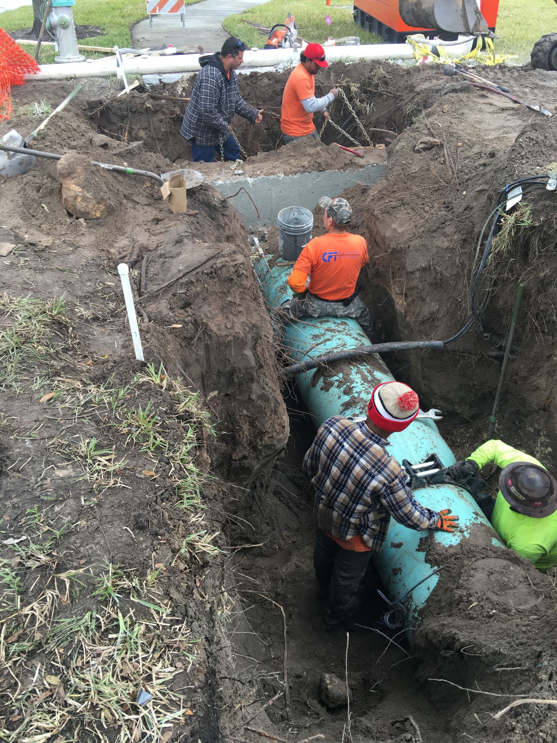 Construction workers in trench working on large pipe.