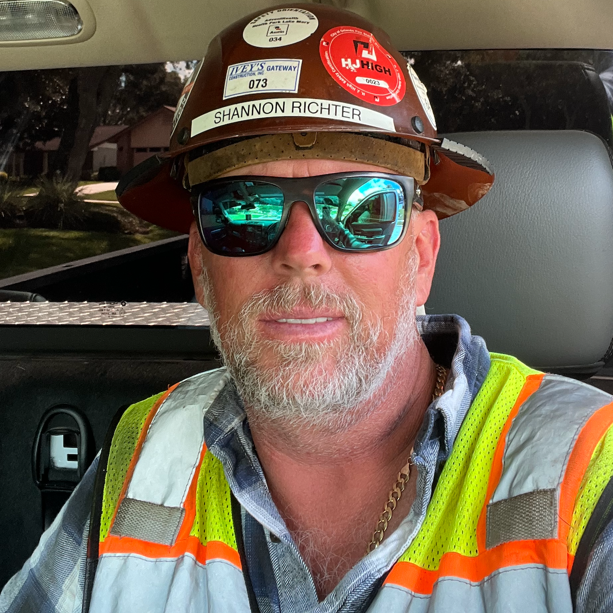 Man wearing hard hat and sunglasses, wearing a high-visibility vest.