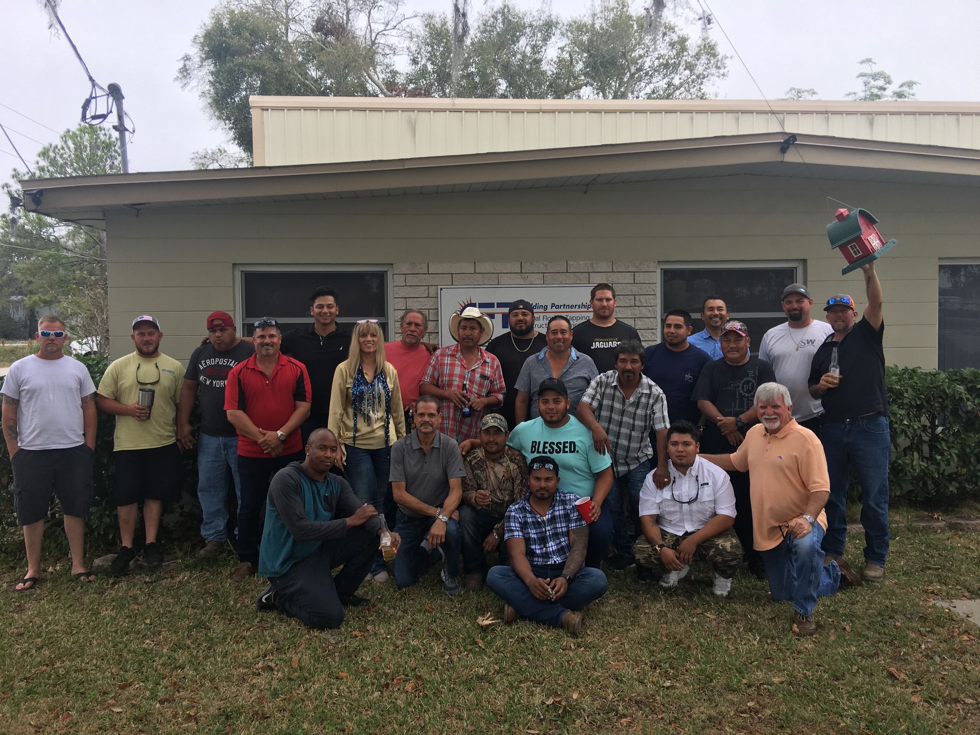 Group of people outside a building. Some are holding drinks, one holds a chainsaw.