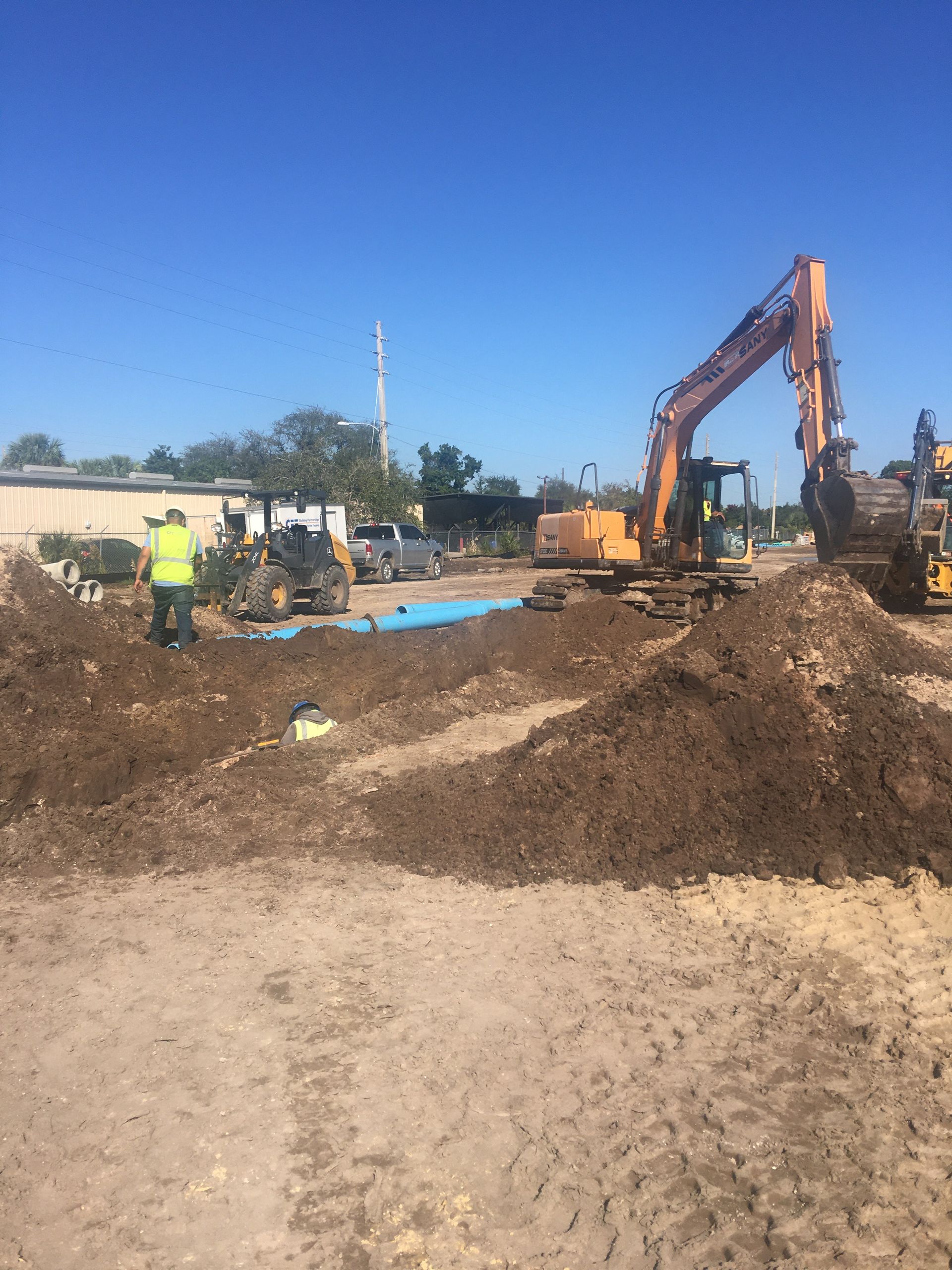 Construction site with an excavator and other machinery, moving earth under a bright blue sky.
