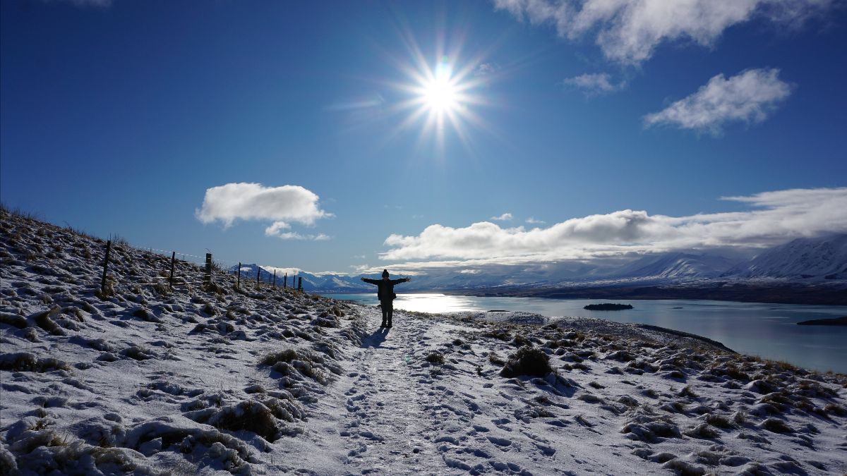 A person is standing in the snow near a lake.