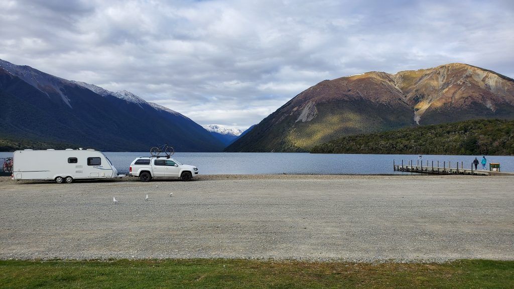 Two rvs are parked on the shore of a lake with mountains in the background.