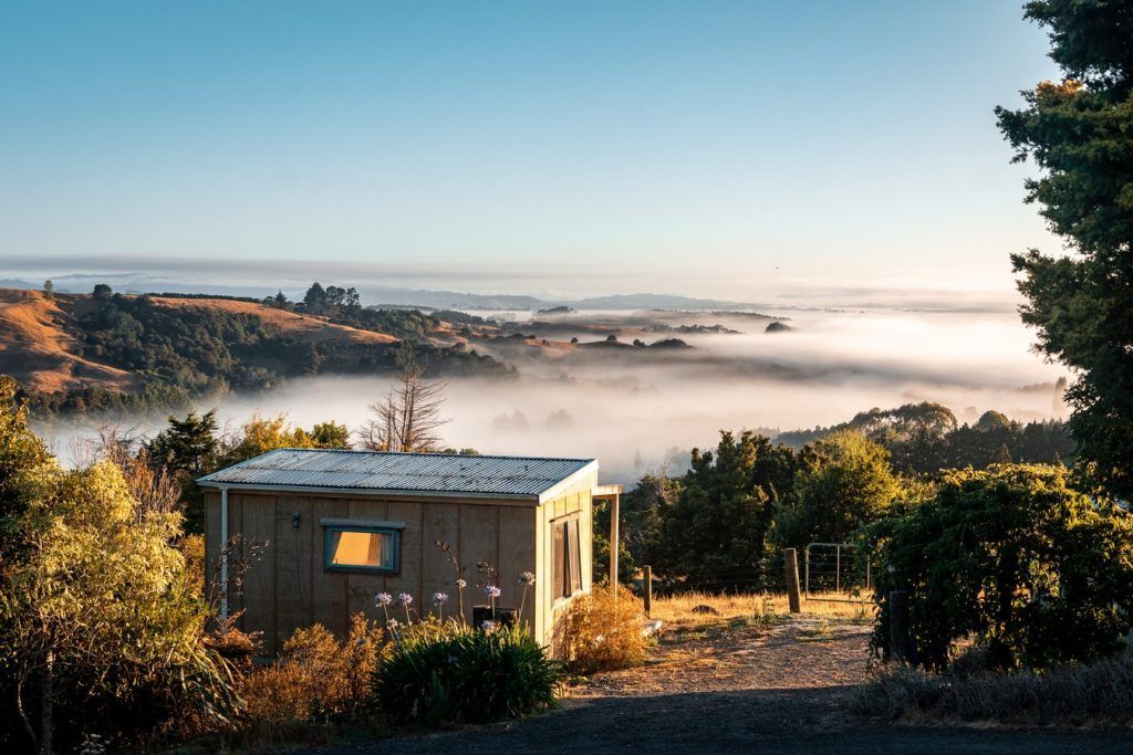 A small house is sitting on top of a hill overlooking a foggy valley.