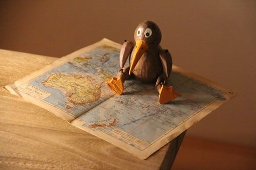 A wooden penguin is sitting on top of an open map.