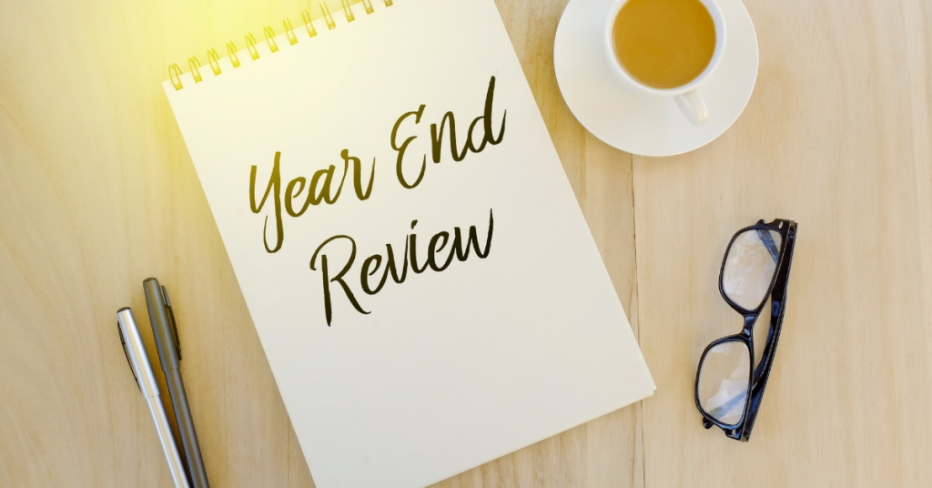 A notebook with the words `` year end review '' written on it is on a wooden table next to a cup of coffee and glasses.