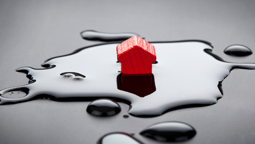 A small red house is sitting in a puddle of liquid.