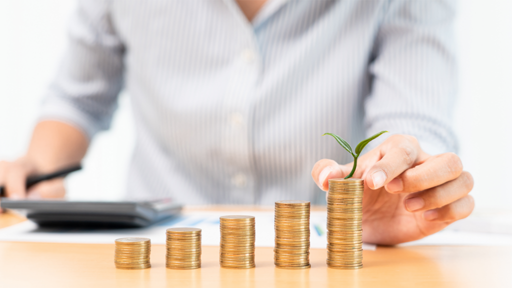 A person is holding a plant growing out of a stack of coins.