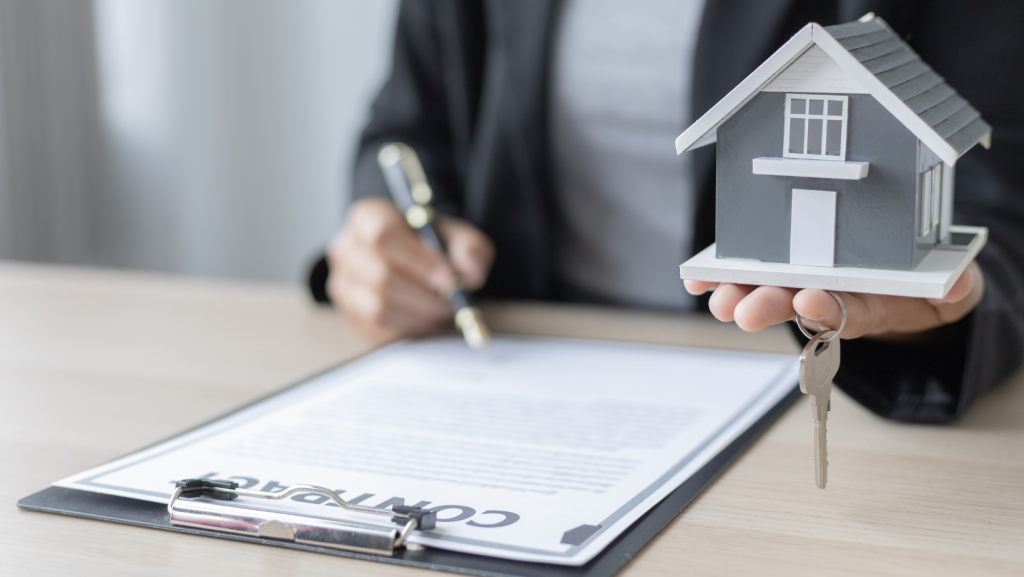 A woman is signing a contract for a house while holding a model house and keys.