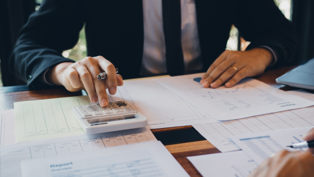 A man in a suit and tie is sitting at a table using a calculator.