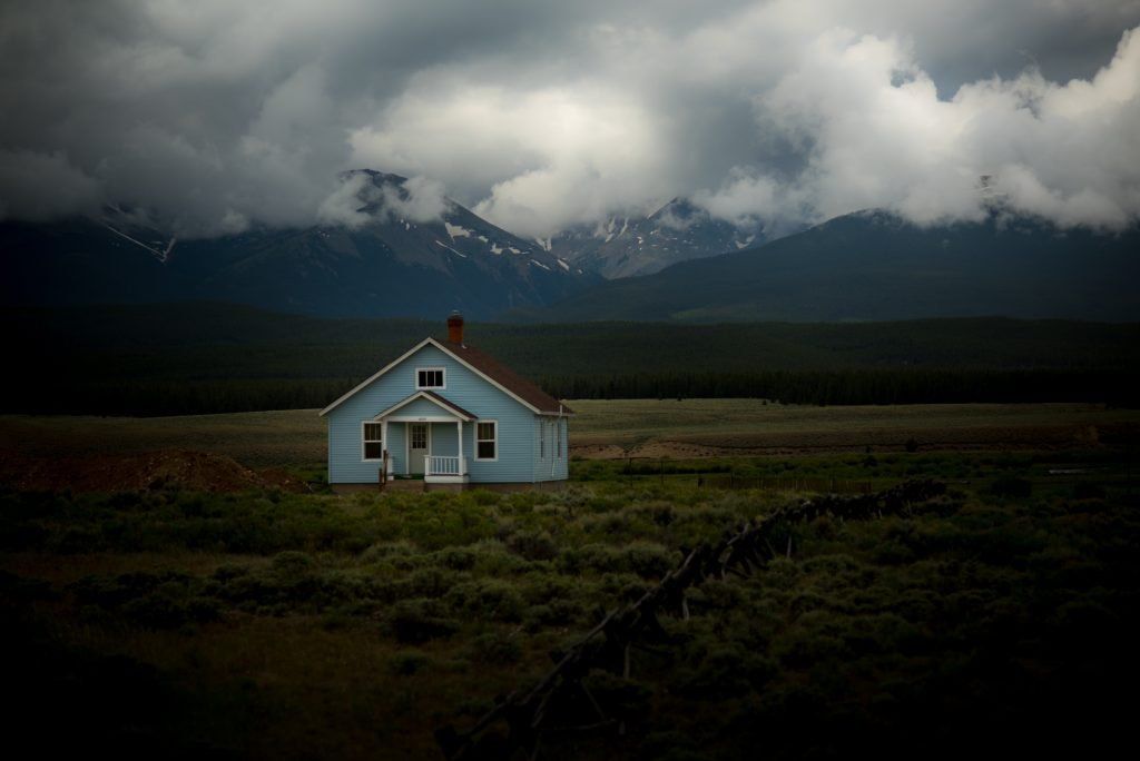 A small house in the middle of a field with mountains in the background