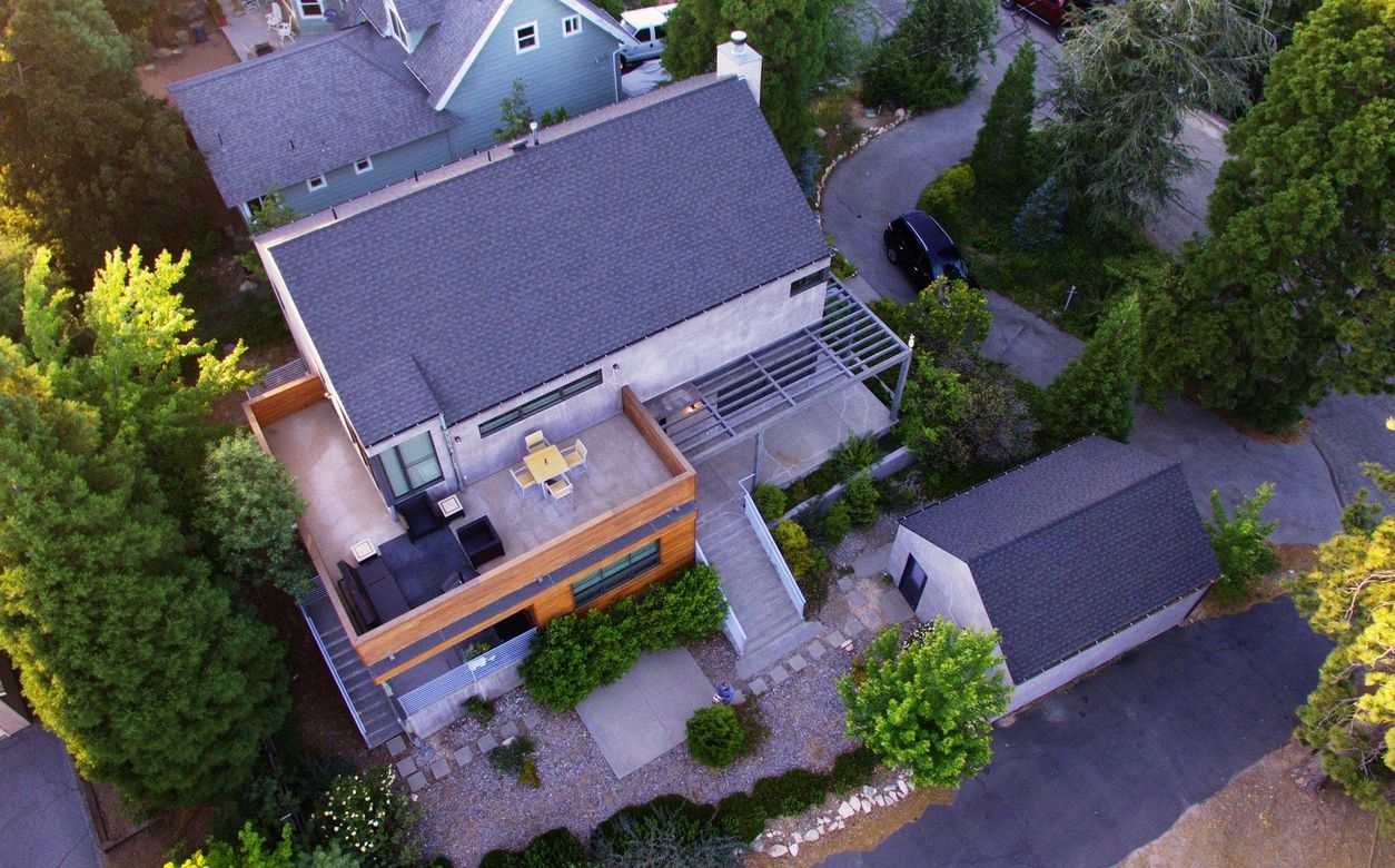 An aerial view of a house with a rooftop deck surrounded by trees.