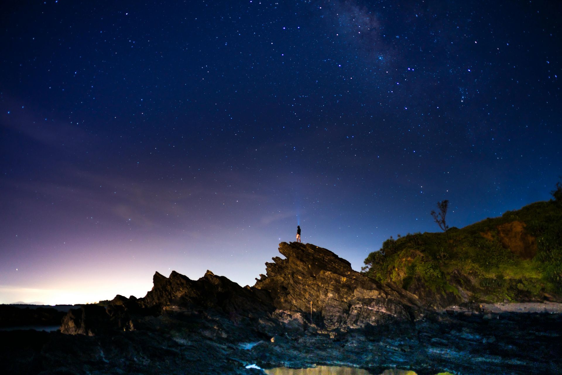A person is standing on top of a rock under a starry night sky.