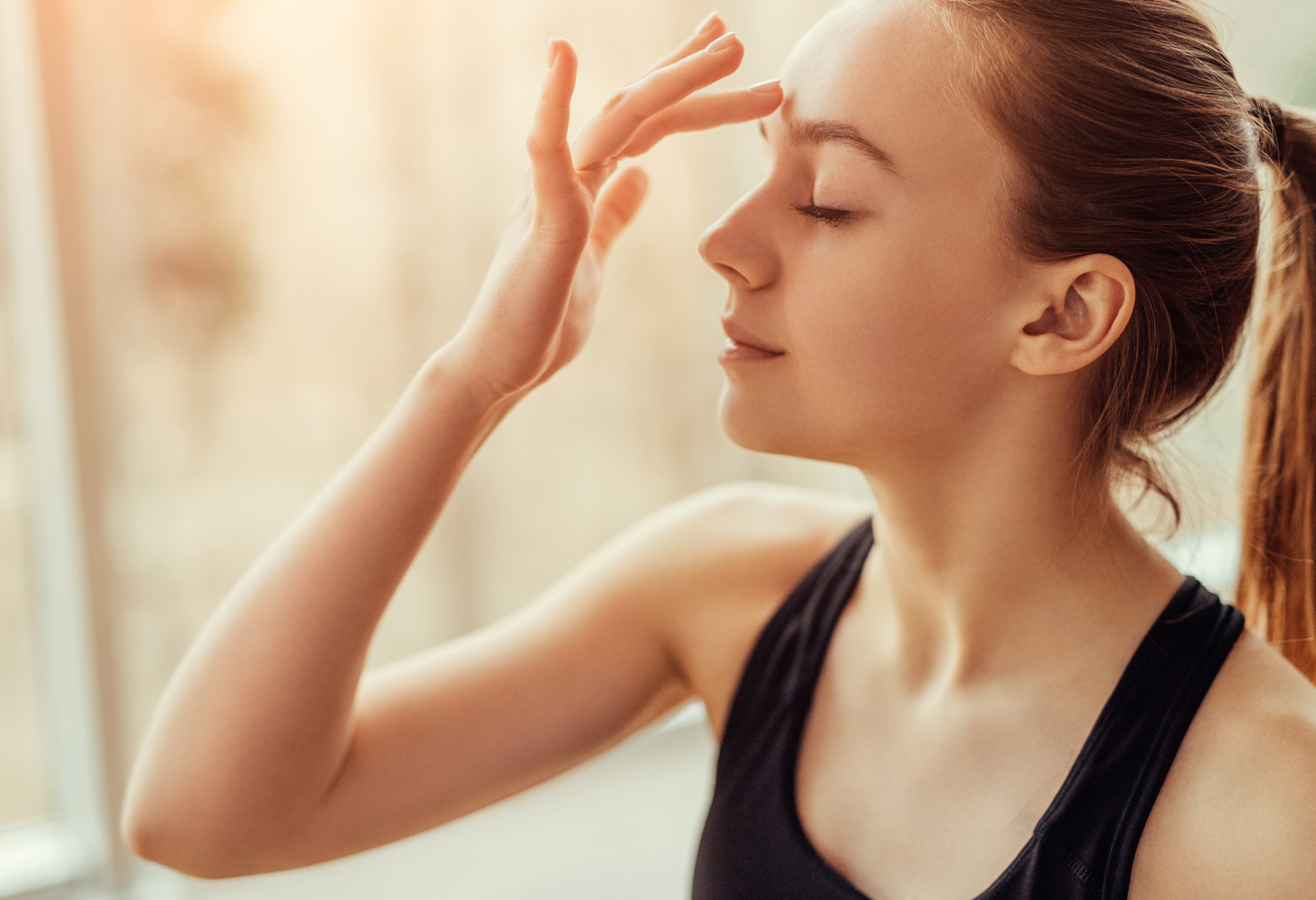 A woman is meditating with her eyes closed and her hand on her forehead.