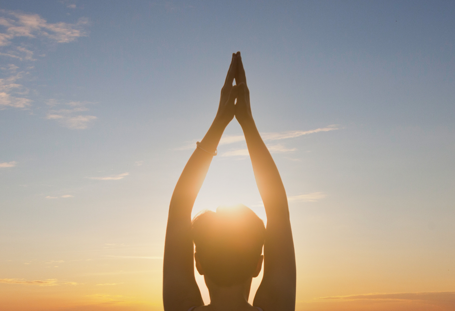 A woman is practicing yoga in front of the sun at sunset.