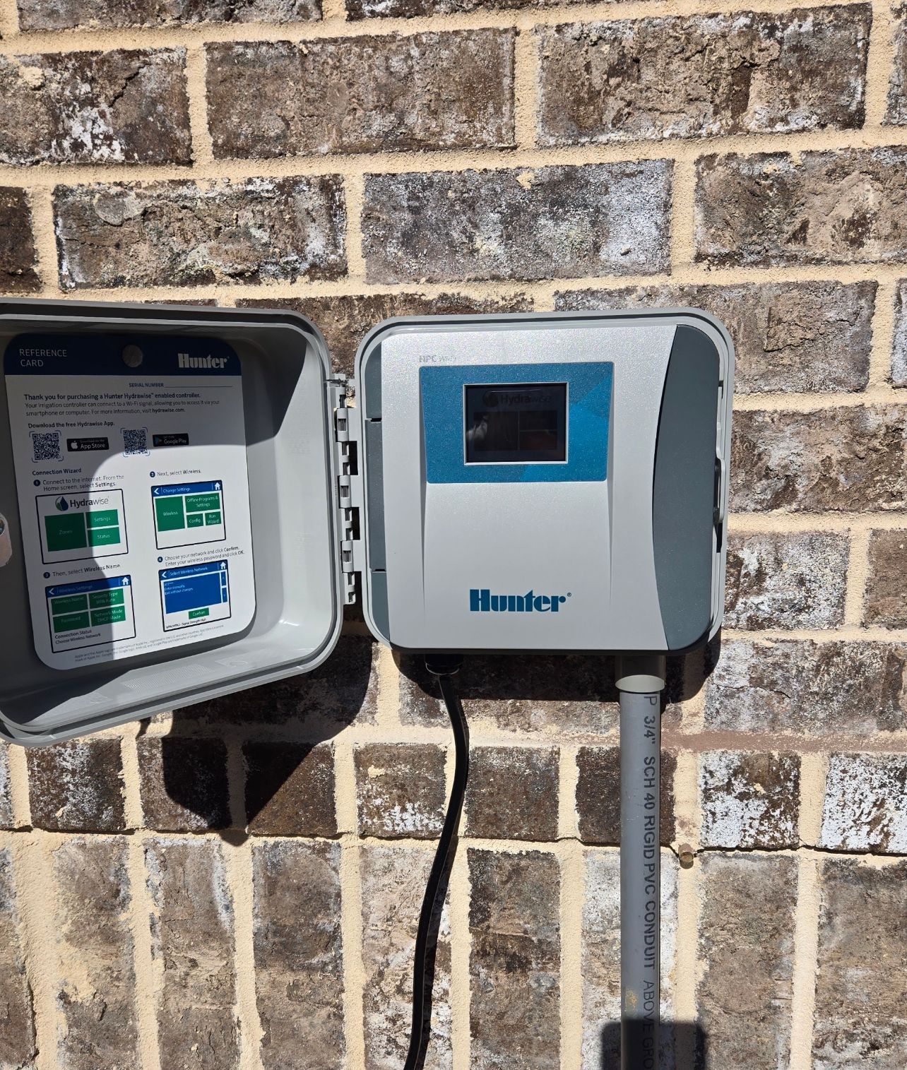 A hunter irrigation controller is mounted on a brick wall.