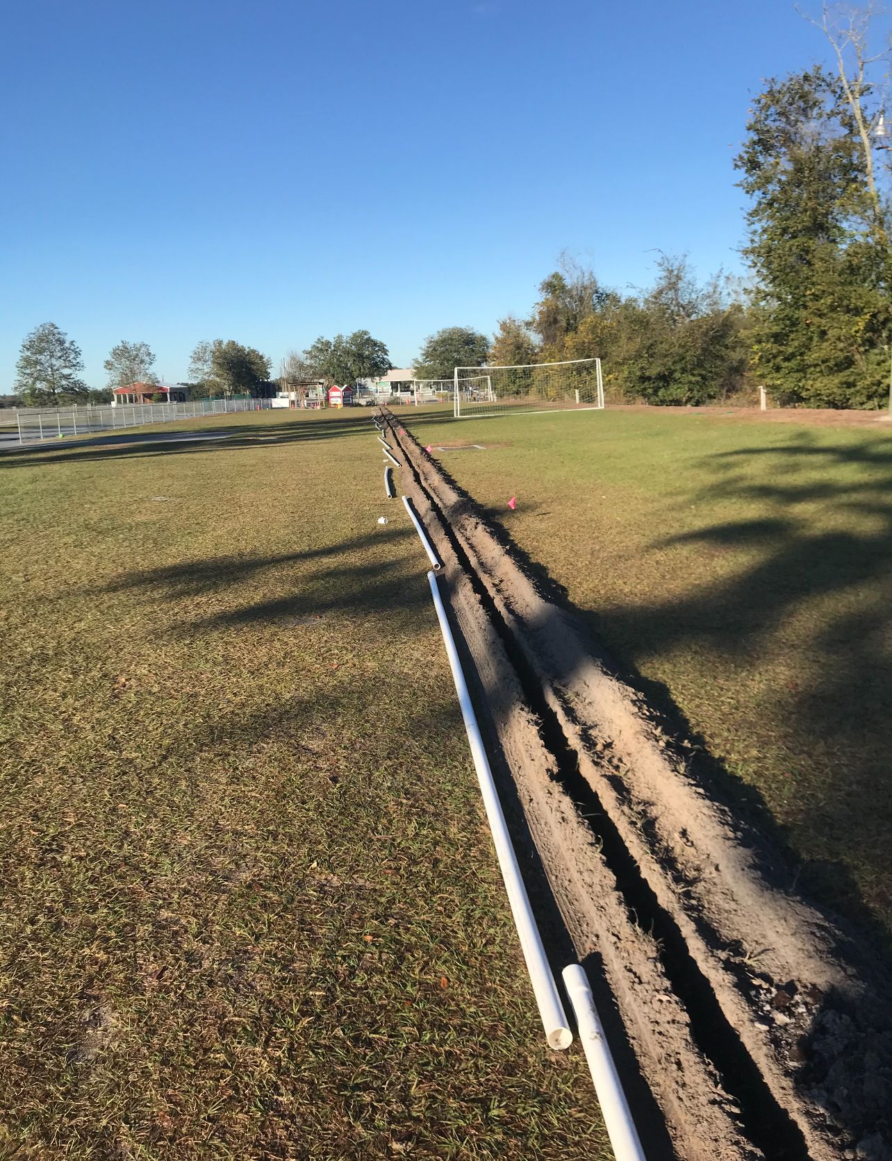 A dirt road going through a grassy field with a blue sky in the background.