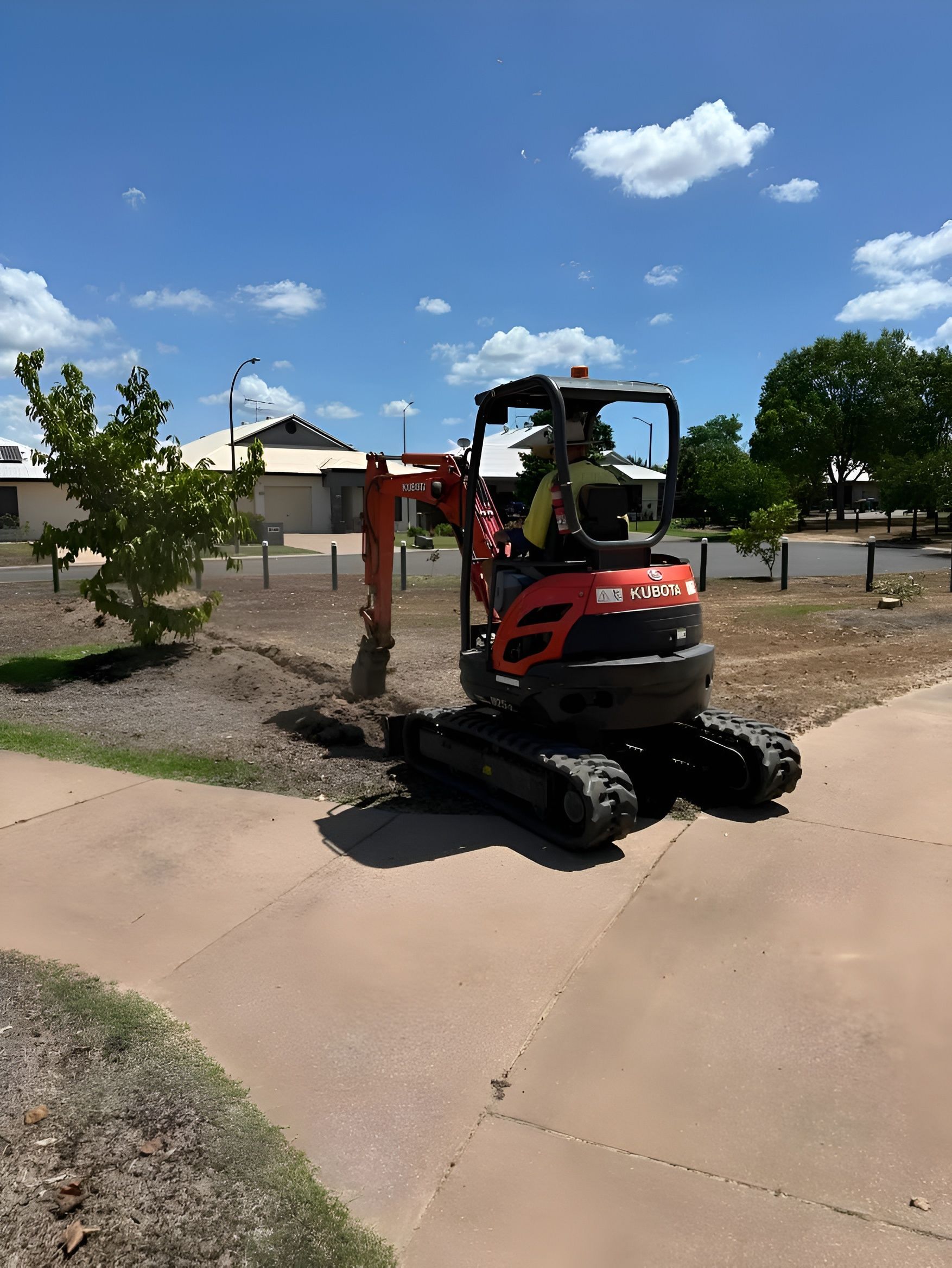 Mini excavator digging in a garden bed near a sidewalk, under a blue sky. — iWater NT Pty Ltd in Yarrawonga, NT