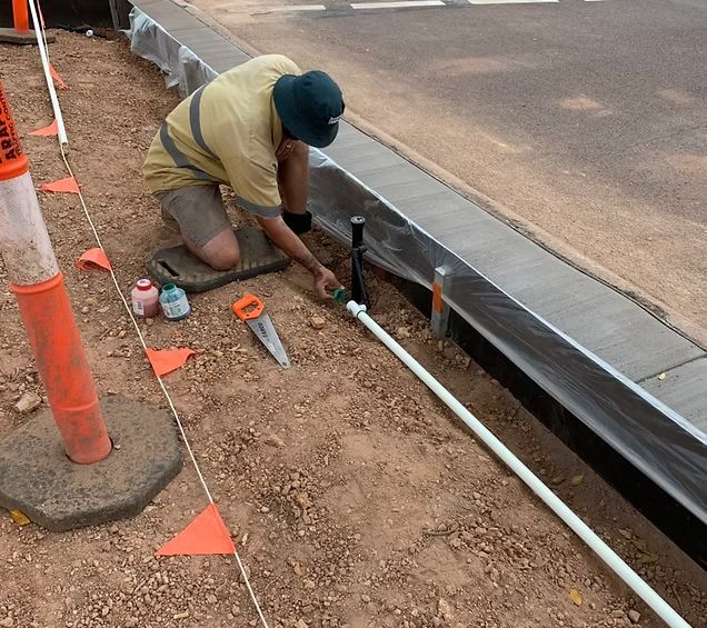 A Worker Kneels, Connecting White Pipe to a Black Pipe Near a Curb — iWater NT Pty Ltd in Yarrawonga, NT