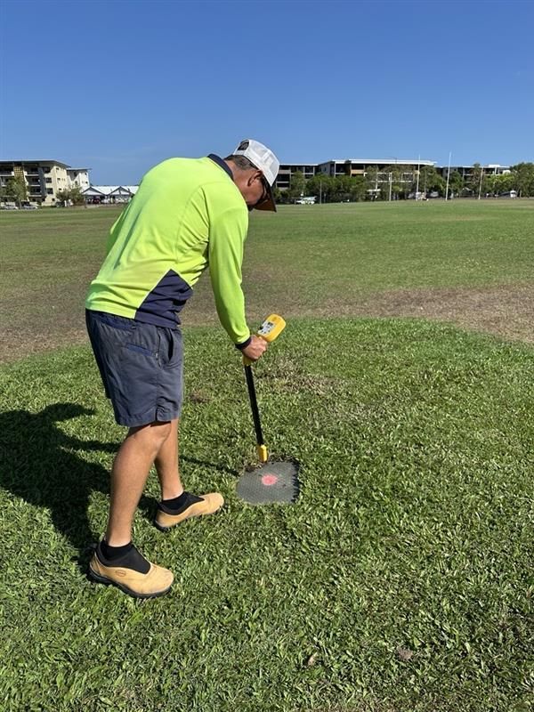 Man in safety vest using a tool on grass field. Bright sun, buildings in the background. — iWater NT Pty Ltd in Yarrawonga, NT