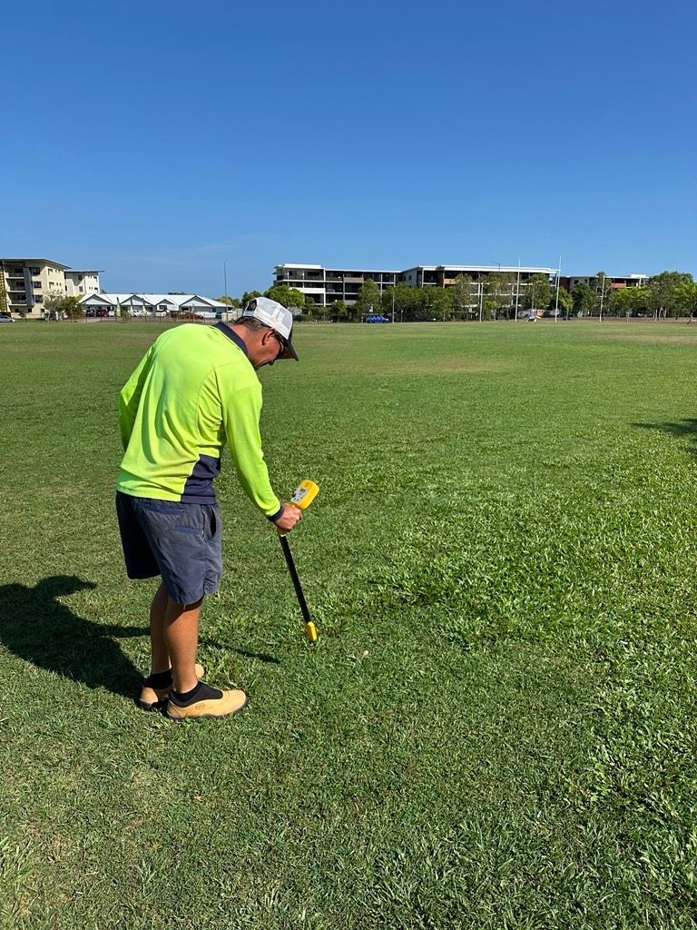 Man in bright yellow shirt using a surveying tool on a grassy field under a blue sky. — iWater NT Pty Ltd in Yarrawonga, NT