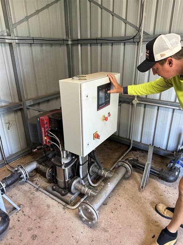 Man in a cap points at a white control panel with a screen and buttons, part of a water pump system. — iWater NT Pty Ltd in Yarrawonga, NT