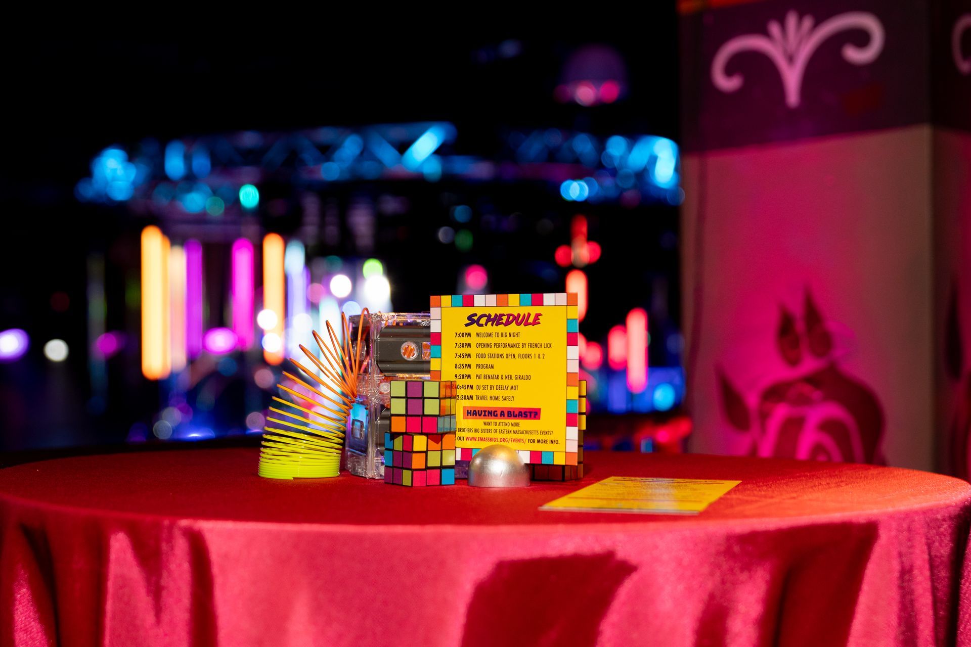 A table set with 80s themed decorations and a schedule sign in a club setting with colorful lights.