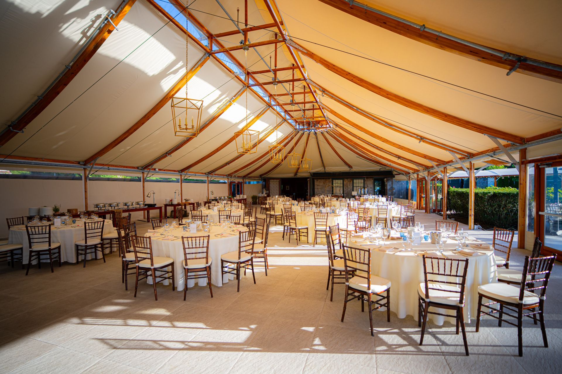 Wedding reception tent with round tables set with white linens and wooden chairs.