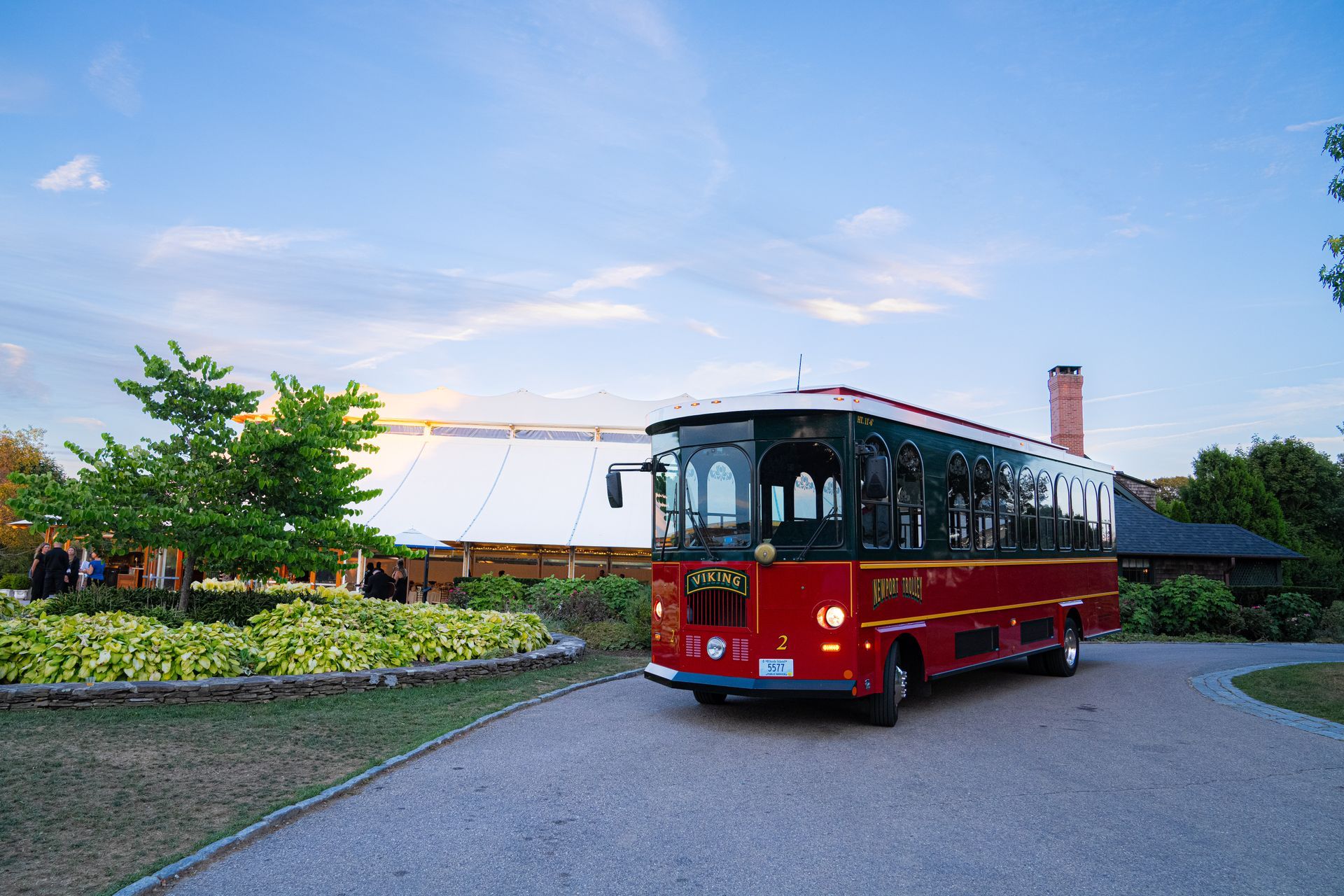 Red trolley on a curved driveway with a white tent and foliage in the background under a blue sky.