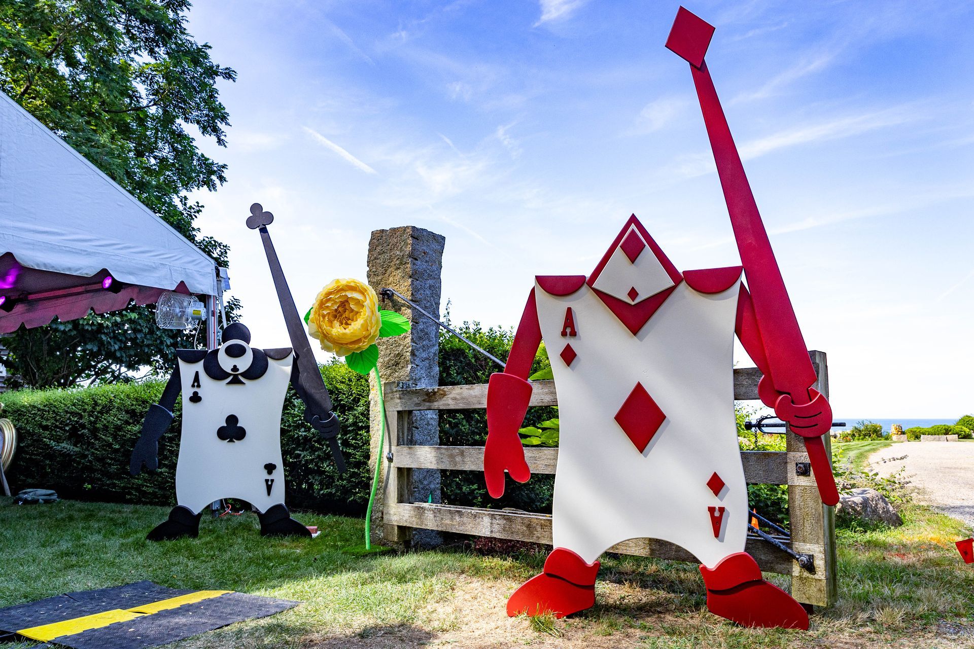 Two large card-shaped figures, one black and one red, stand in a grassy area under a bright blue sky.