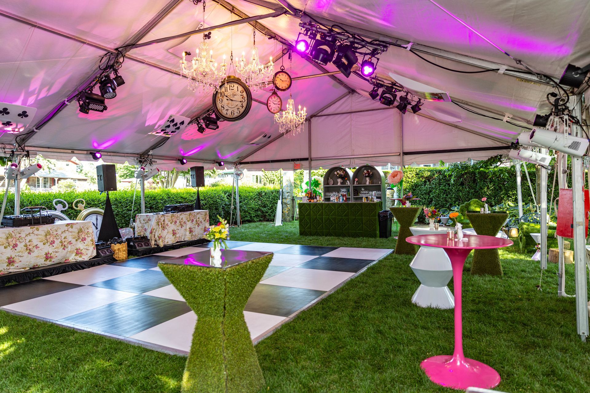 Party tent with dance floor, tables, bar, and decor. Lit with pink lights, set on grass.