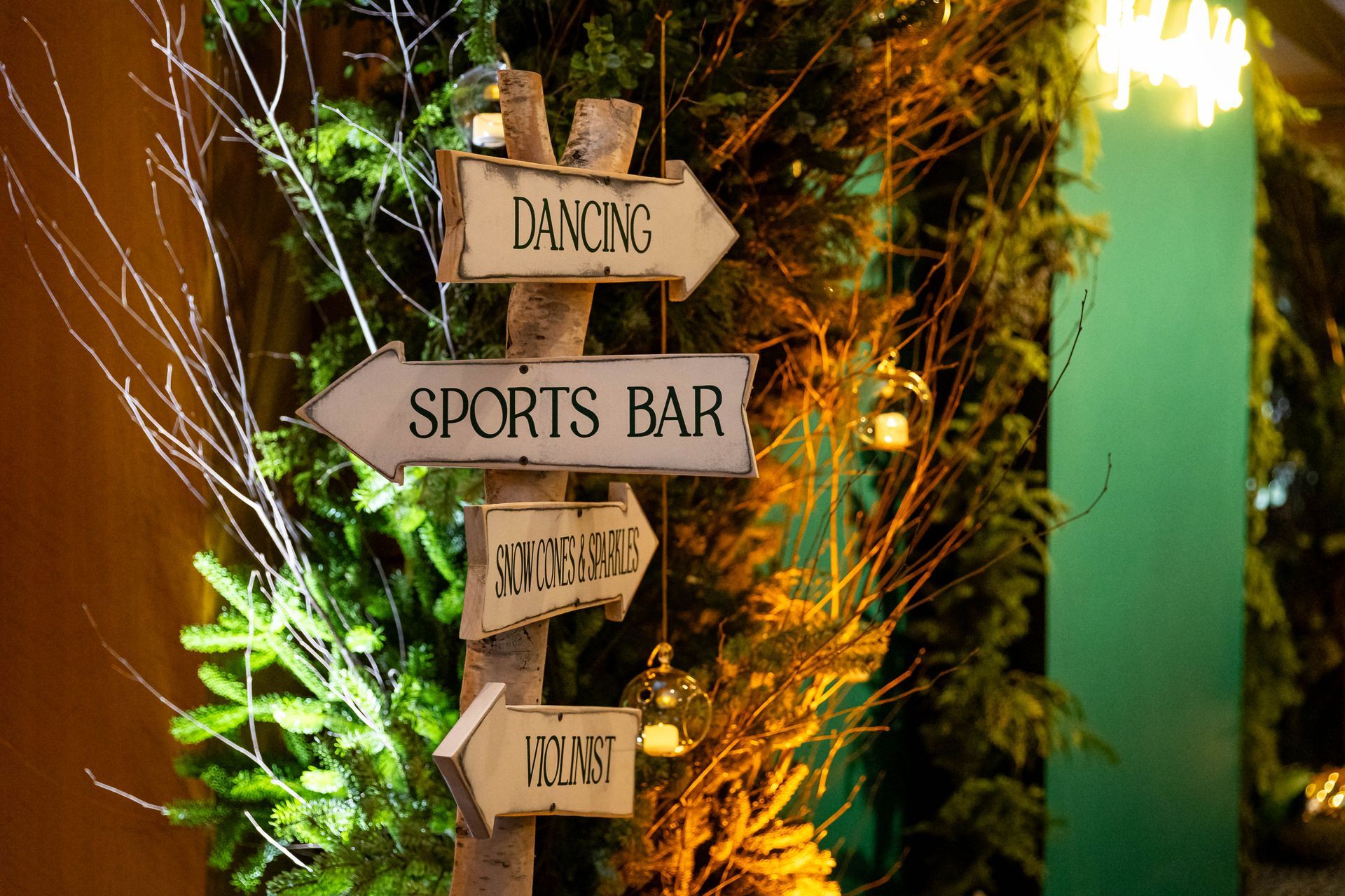 Signpost directing to dancing, sports bar, karaoke, and holidays, decorated with branches and lights.