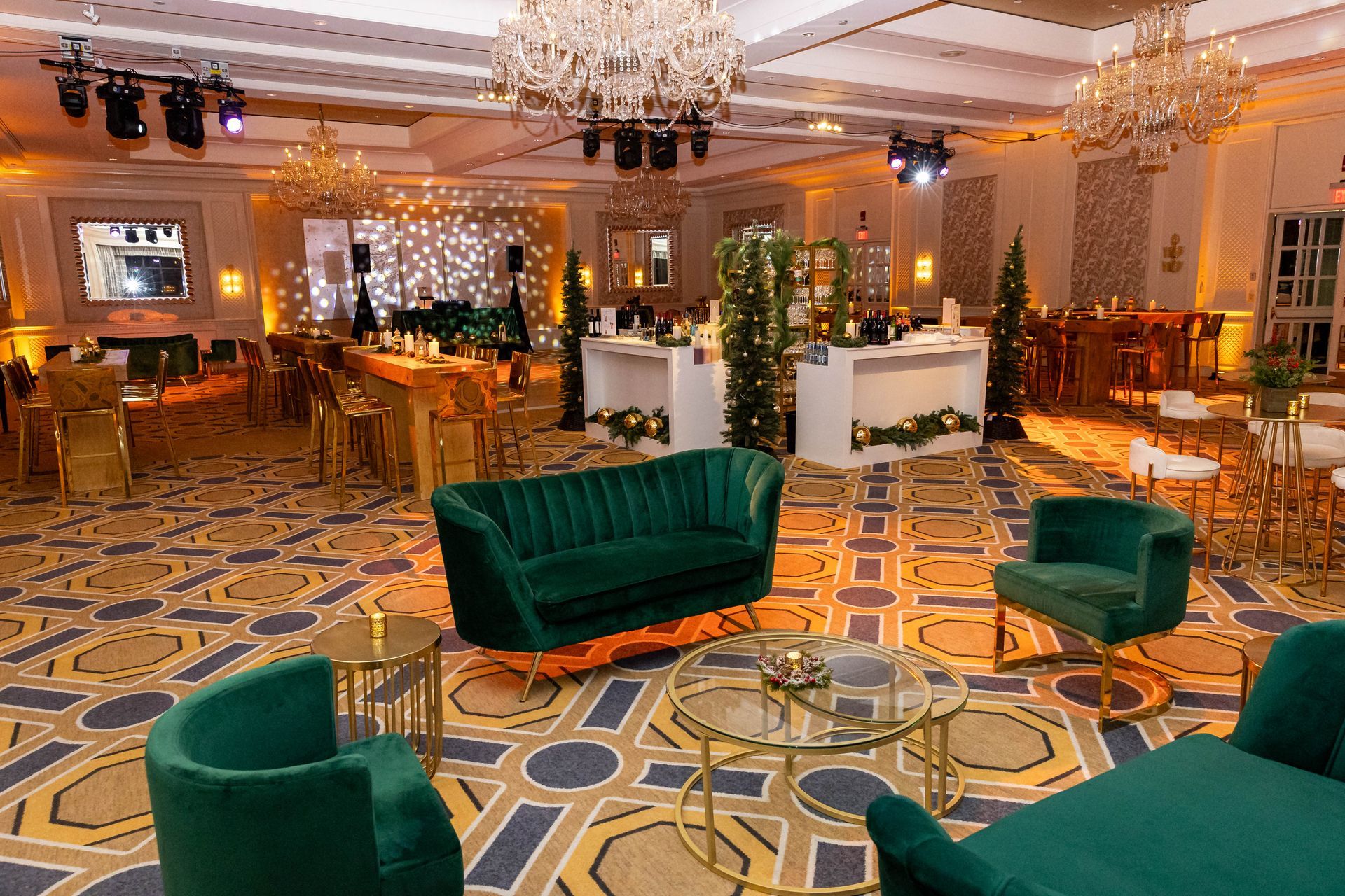 An elegant ballroom with emerald green seating, gold accents, and chandeliers, set for an event.
