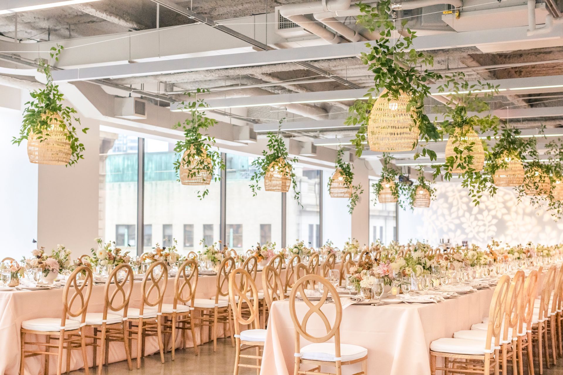 Long table set for a wedding reception, with hanging floral baskets and light-colored decor.