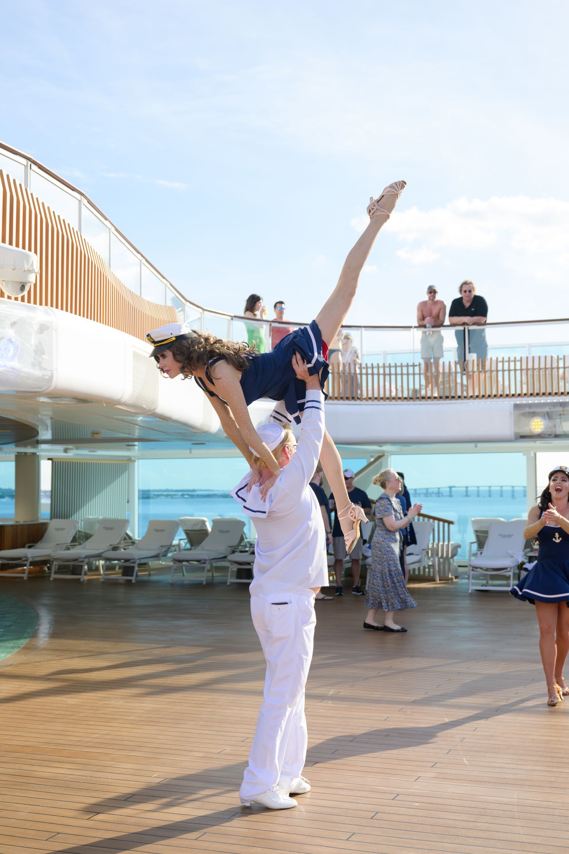 Two people in sailor costumes perform acrobatic dance on a cruise deck, near a pool.