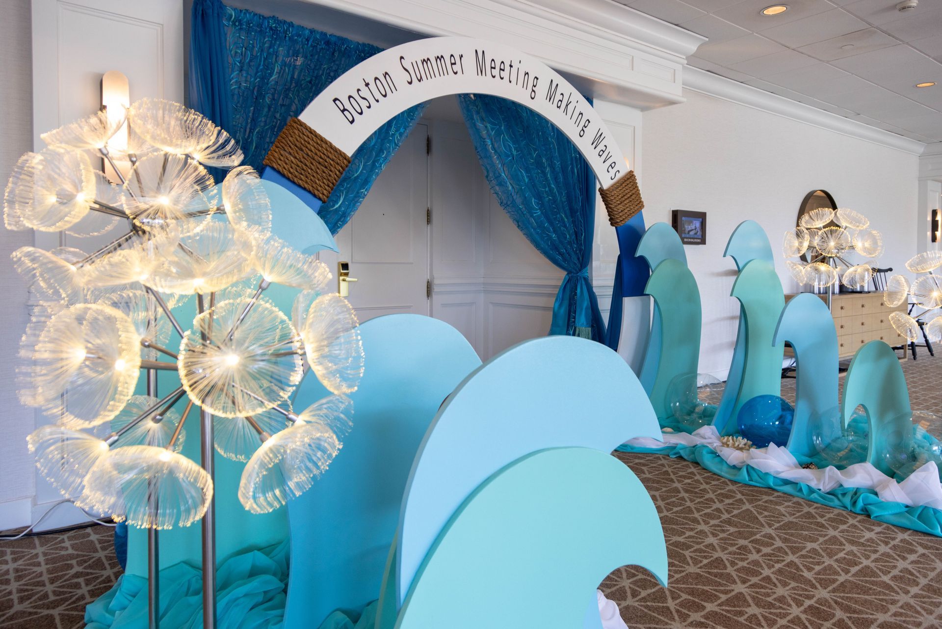 Ocean-themed event entrance. Blue wave cutouts, arch with text, sparkly decorations.