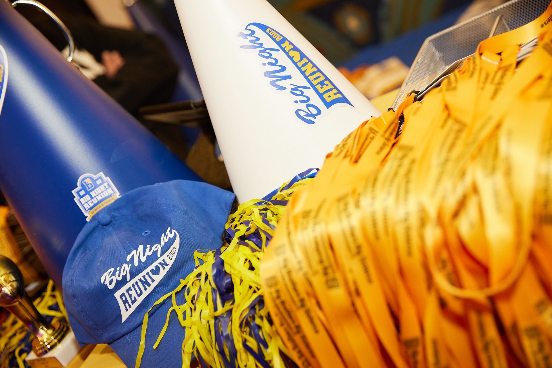 Blue and white Big Night Reunion cheerleading megaphones, blue cap, and yellow ribbons.