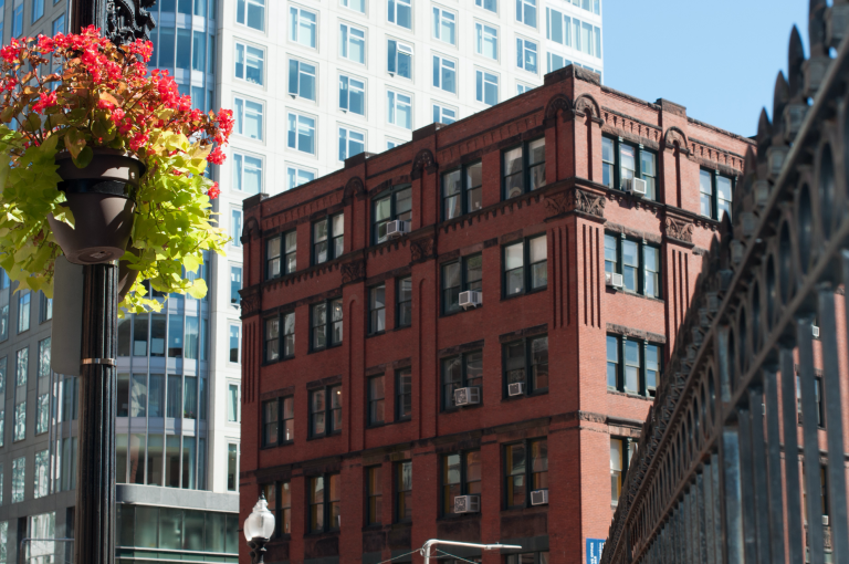 A brick building with a lot of windows is in the middle of a city.