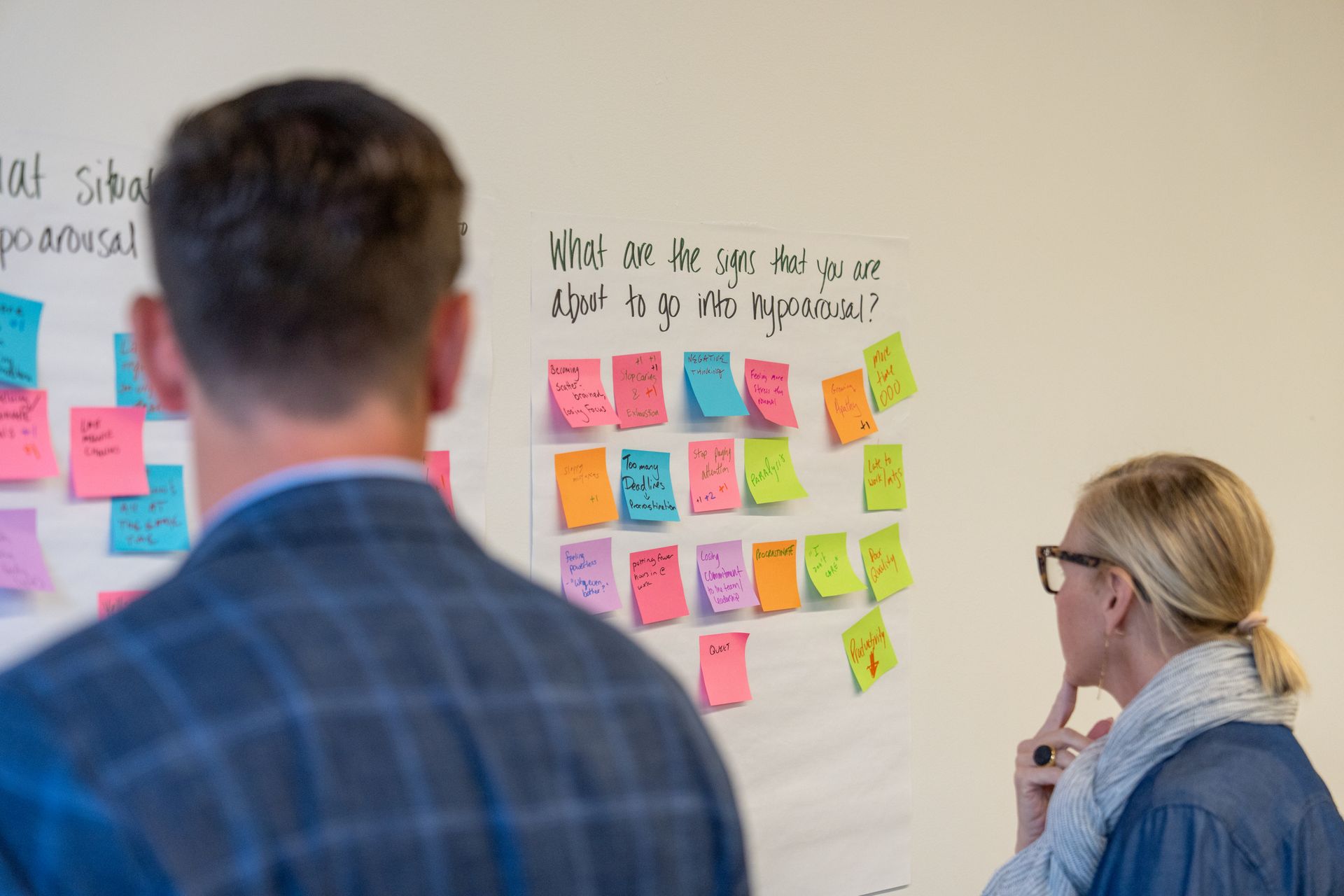 Two people in an office looking at a whiteboard covered in colorful sticky notes, brainstorming ideas.