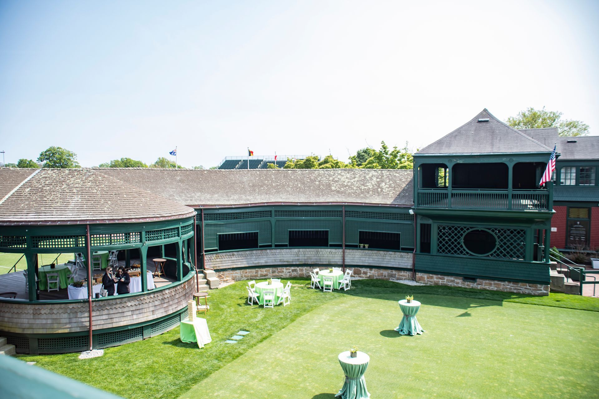 Green building with outdoor seating, lawn, tables, and guests on a sunny day.