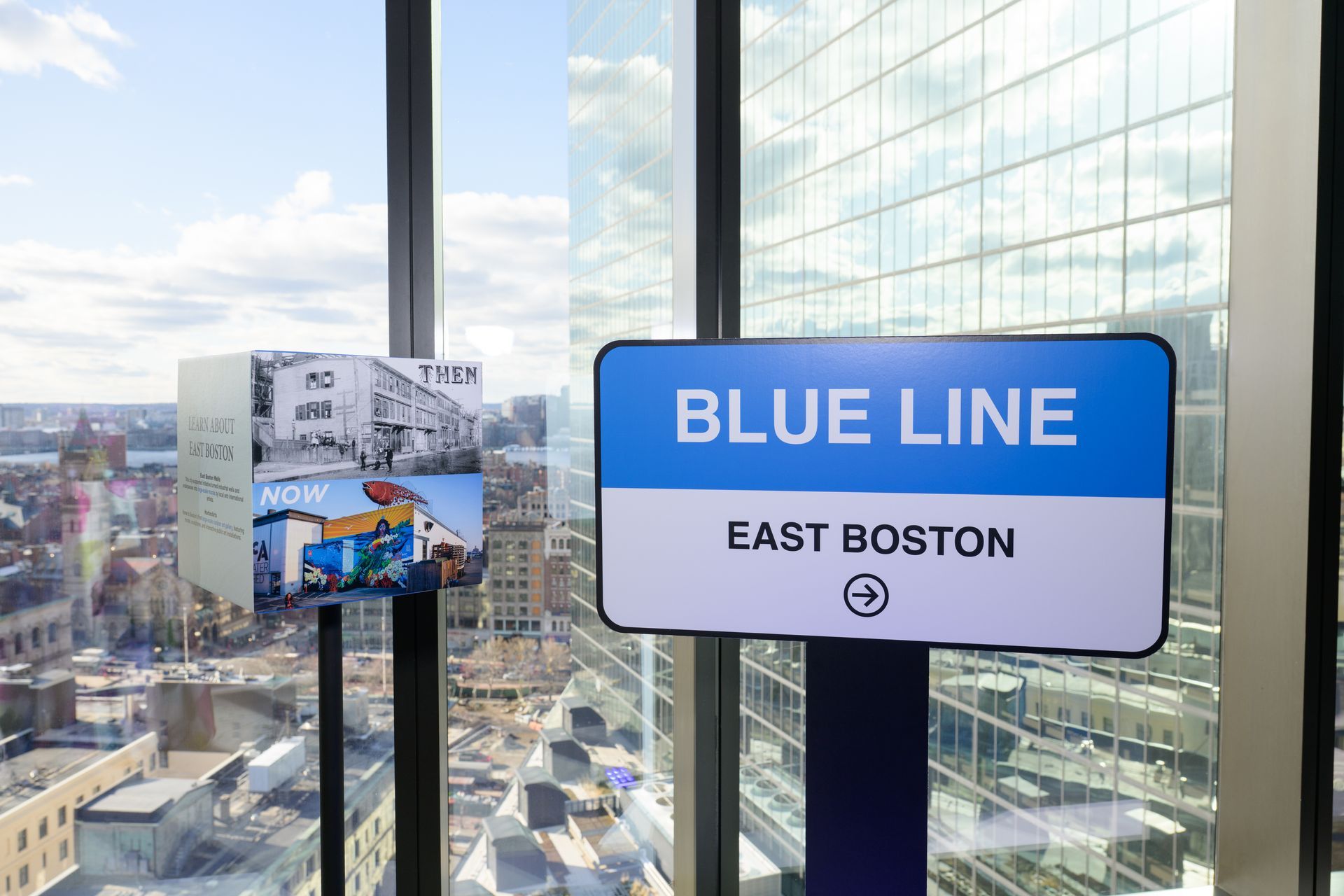Sign for Blue Line subway in East Boston, with a city view from a window.